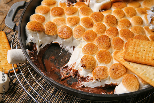 Frying pan with tasty S'mores dip and crackers on wooden table, closeup