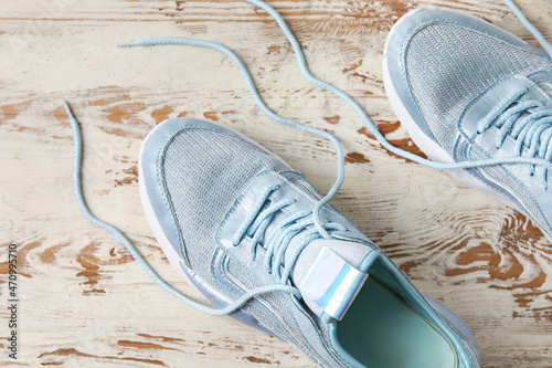 Pair of sportive shoes with untied laces on light wooden background, closeup photo