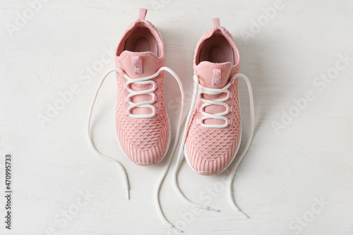 Pair of sportive shoes with untied laces on light wooden background
