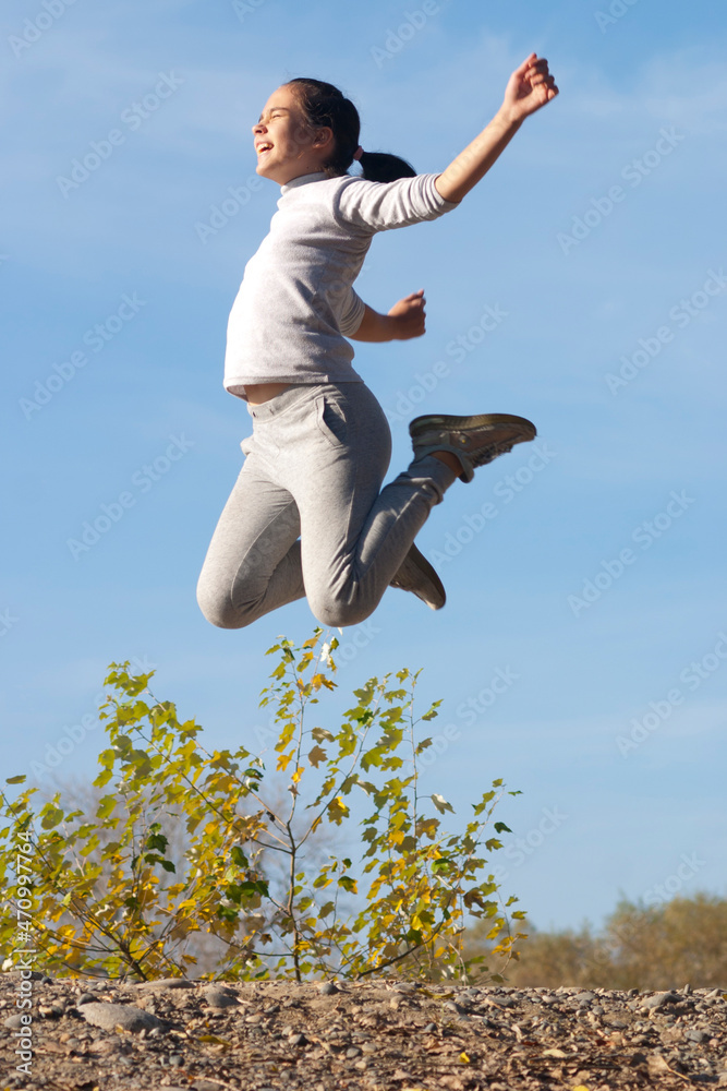Girl in a jump. A pre-teen girl (eleven years old) jumps high outdoors in a park. Autumn. Sky is blue. One person Girl in a jump. A pre-teen girl (eleven years old) jumps high outdoors in a park. Autumn. Sky is blue. One person