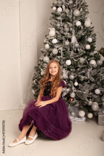 a girl in a dress sits at a festive party at the Christmas tree in a beautiful dress © Marina Chernivetskay