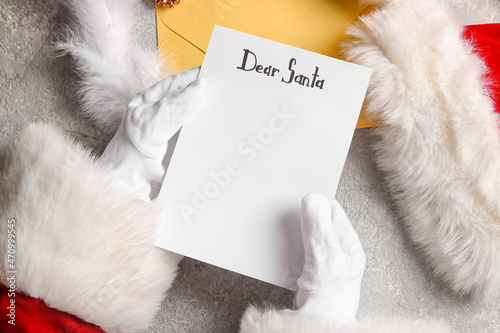 Santa Claus holding blank wish list letter on grey table with Christmas decor, closeup