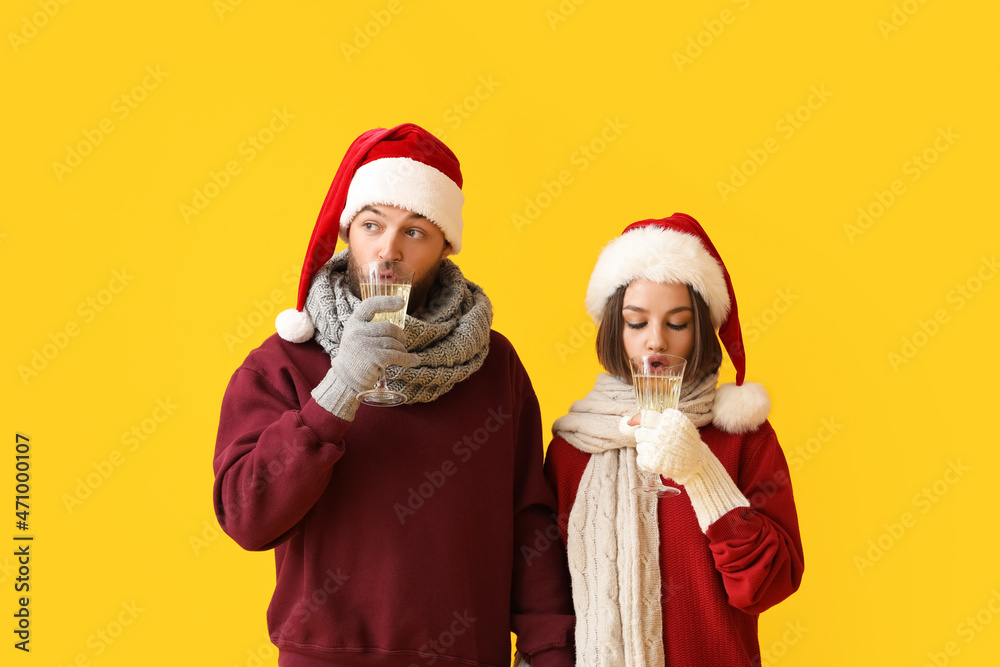 Young couple in Santa Claus hats and with glasses of champagne on color background Young couple in Santa Claus hats and with glasses of champagne on color background