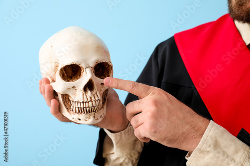 Male graduate pointing at human skull on blue background, closeup © Pixel-Shot