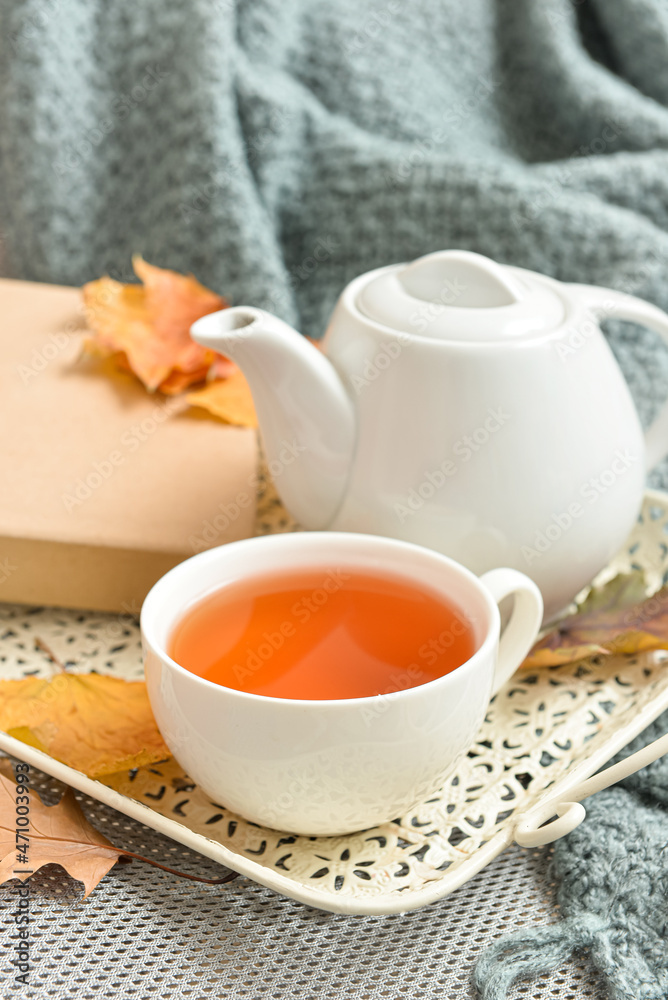 Tray with tea pot, cup of hot beverage and autumn leaves on sofa in room Tray with tea pot, cup of hot beverage and autumn leaves on sofa in room