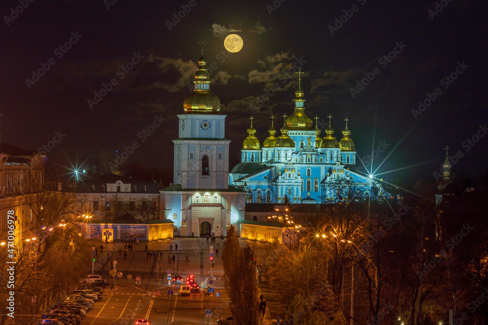 View of the illuminated St. Michael's Cathedral against the background of the sky with the rising full moon and clouds.