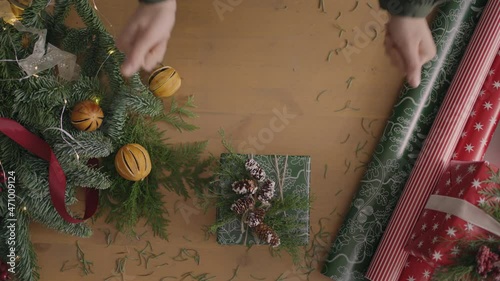 top view plan. Fully visible the table with the decorations. hands put and finalize Christmas gift wrapped in craftool paper on a wooden table. Bandaging tape and tied bow. photo