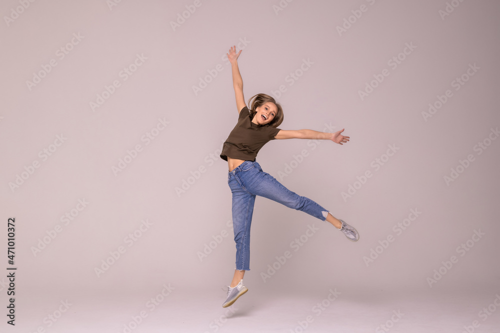 Smiling young woman jumping in air with raised fists over white background