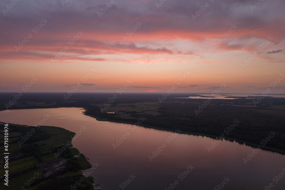 Aerial landscape of the lakes surrounded by the green forest. Pastel orange clouds during summer sunset.