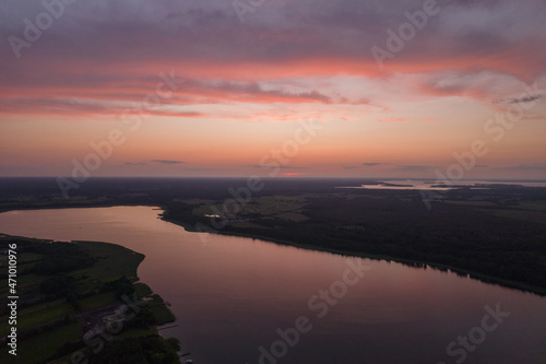 Aerial landscape of the lakes surrounded by the green forest. Pastel orange clouds during summer sunset.