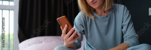 Young woman in pajamas sitting in bed with mobile phone in hand