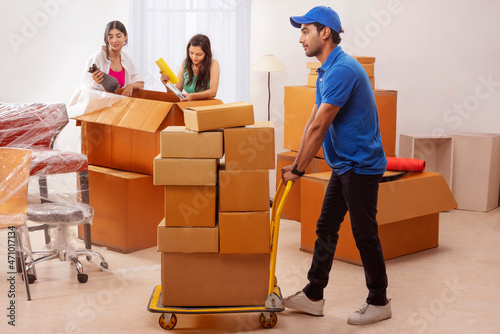Girls busy with packing while the delivery boy moving boxes to new house photo