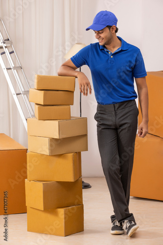 Delivery boy in uniform standing with leaning on cardboard boxes