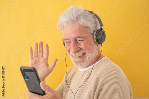 Happy senior white-haired man wearing headphones while using mobile phone for video calling. Elderly grandfather enjoying tech and social © luciano