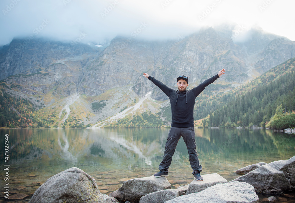 Young tourist man in a cap with hands up on the top of the mountains
