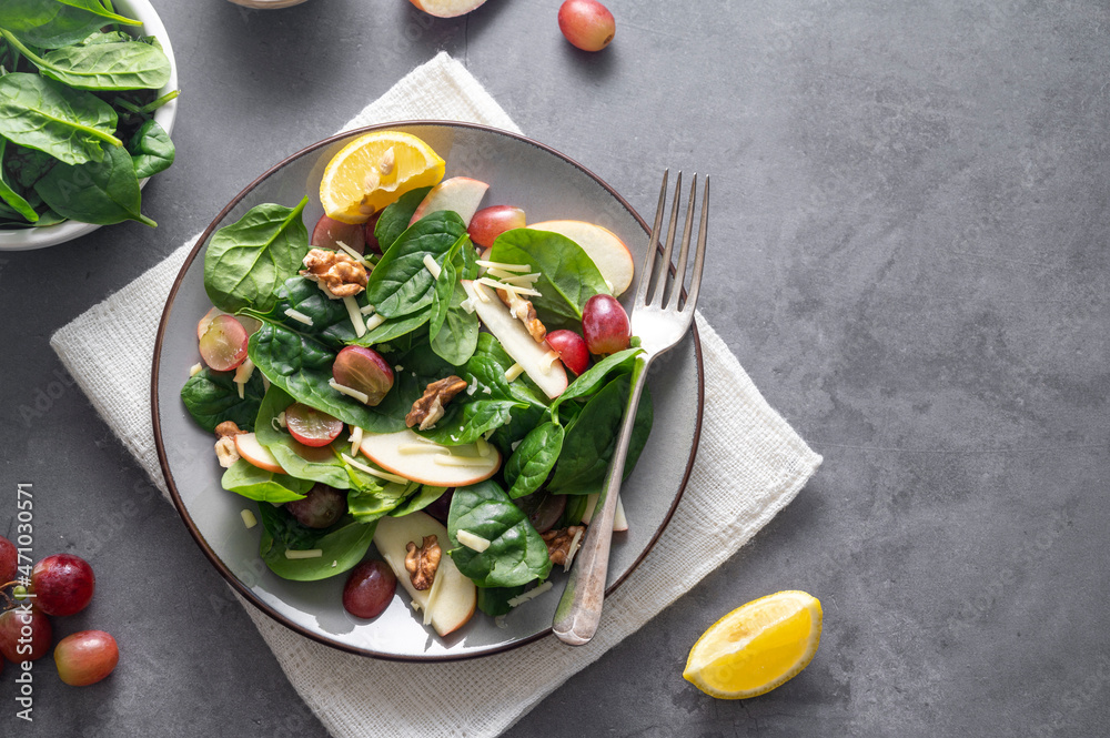 Healthy salad with red apple, wallnuts, grapes and fresh spinach leaves. Dark background