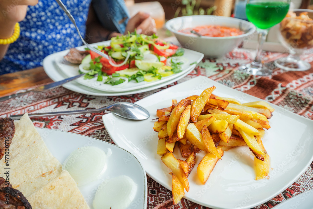 Delicious and unhealthy fatty French fries on a plate in a restaurant among other dishes Delicious and unhealthy fatty French fries on a plate in a restaurant among other dishes
