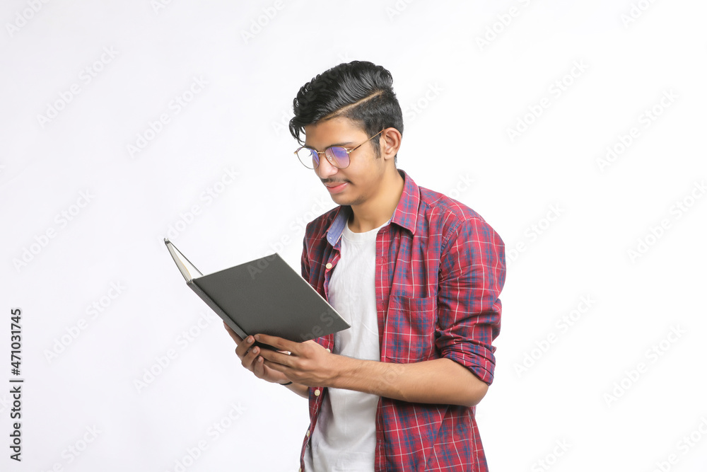Indian college student standing with bag and reading dairy over white background. Indian college student standing with bag and reading dairy over white background.