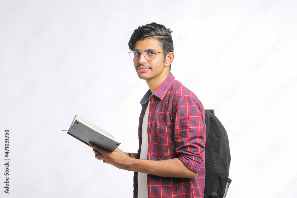 Indian college student standing with bag and reading dairy over white background. Indian college student standing with bag and reading dairy over white background.