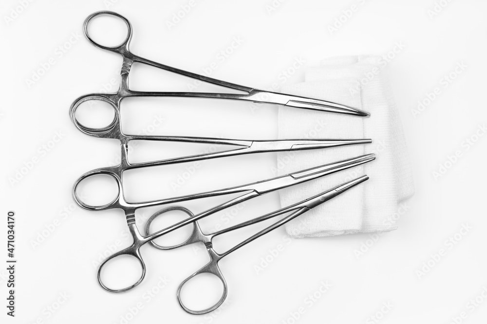 Lot of stainless surgical needle drivers lying on white sterile gauze swab. Medical instruments needle holders on white background. Healthcare and medicine concept. Flat shot, selective focus Lot of stainless surgical needle drivers lying on white sterile gauze swab. Medical instruments needle holders on white background. Healthcare and medicine concept. Flat shot, selective focus