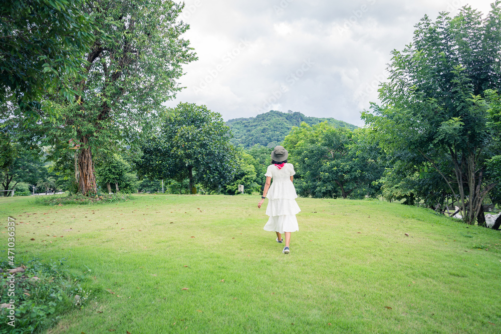 Women in the white dress are walking on the green grass, see the beauty of the tree. Mountains and sky in the morning.