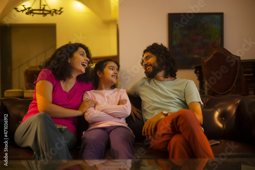 Couple with their daughter having fun in living room while sitting on sofa