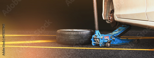 White automobile are lifted by a car jack and a wheel set on an asphalt road with a black background,copy space