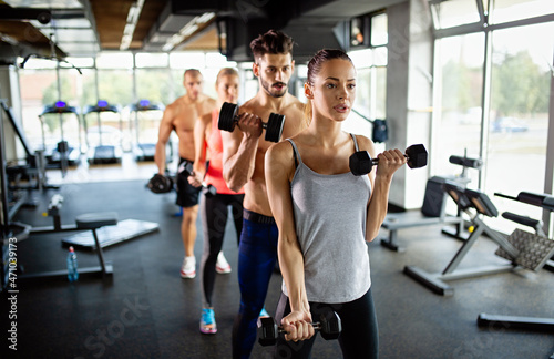 Group of athletic young people in sportswear with dumbbells exercising at the gym