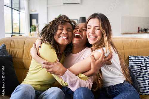 Three happy friends hugging smiling.Funny women together celebrating sitting on the living room sofa