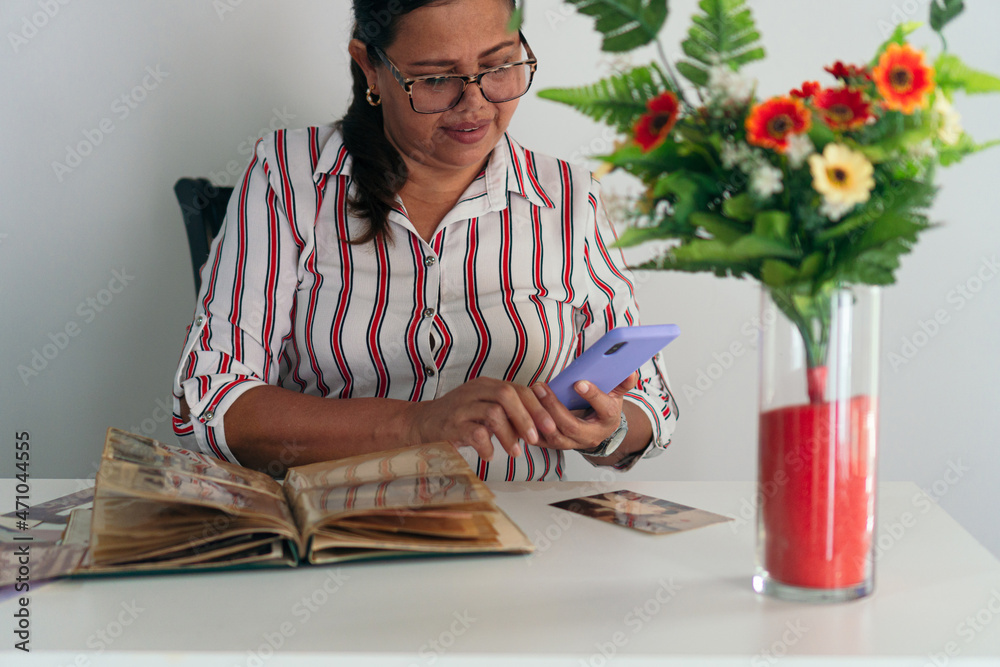 Latin woman looking at her childhood photo album while sitting at the table in her home. Latin woman looking at her childhood photo album while sitting at the table in her home.