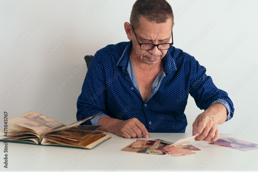 Latin man sitting at the table at home looking at her photo album Latin man sitting at the table at home looking at her photo album