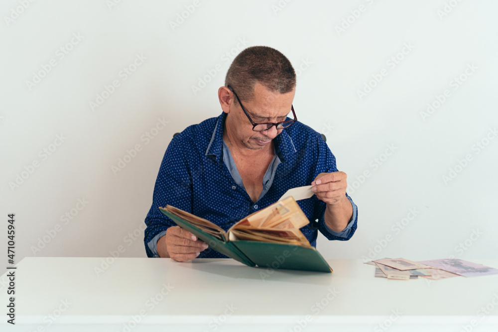Older man sitting at the table at home looking at her photo album Older man sitting at the table at home looking at her photo album