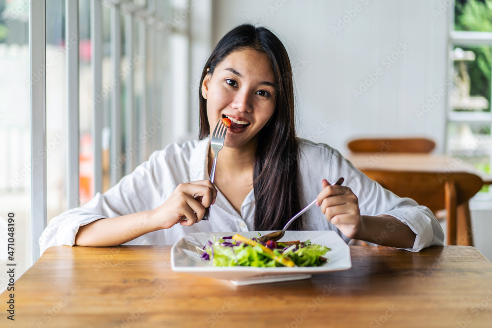 Portrait of attractive asian smiling young woman eating salad in restaurant, A young happy girl having a healthy lunch