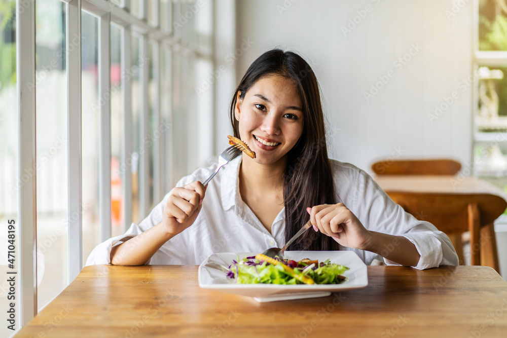 Portrait of attractive asian smiling young woman eating salad in restaurant, A young happy girl having a healthy lunch Portrait of attractive asian smiling young woman eating salad in restaurant, A young happy girl having a healthy lunch