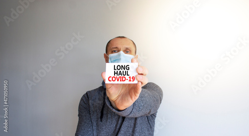 COVID-19 long-haul covid symptoms symbol. White card, words Long haul covid-19. A young man in a grey wear and medical mask. Beautiful white background. COVID-19 long-haul covid symptoms concept. photo