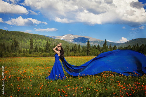 A beautiful woman of Asian appearance in a blue dress walks in a green meadow with orange flowers in the Altai mountains in summer. concept beauty, tourism.
