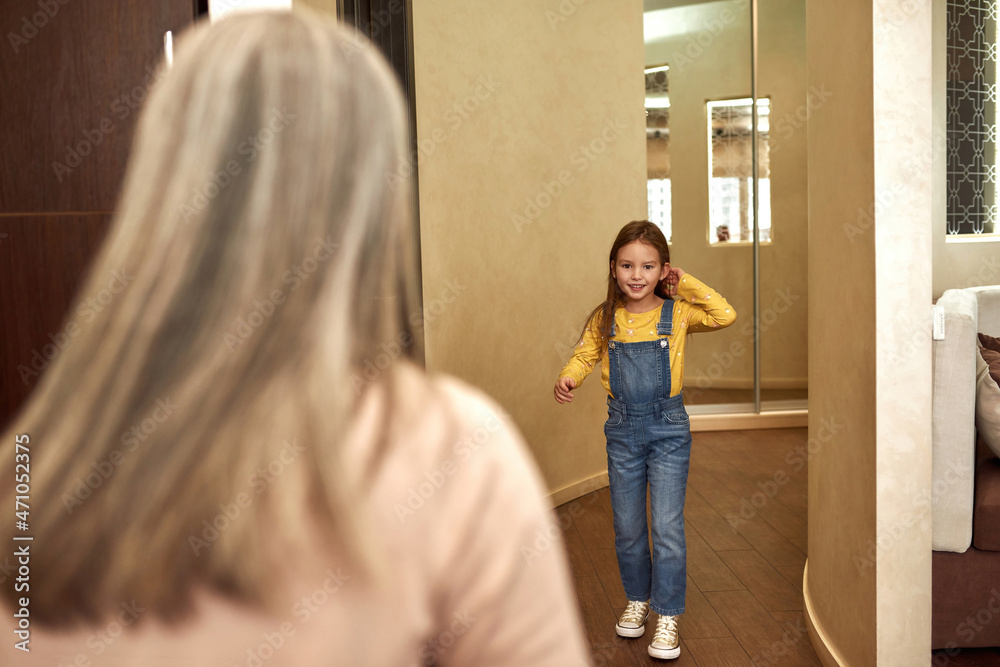 Back view elder woman welcoming little girl at home Back view elder woman welcoming little girl at home