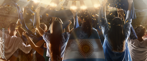 Back view of football, soccer fans from Argentina cheering their team with blue-white state flags and scarfs at crowded stadium. © master1305