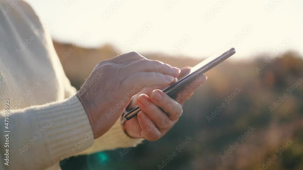 Close up of a old woman hand using mobile smart phone outside on sunny summer day. Abstract warm landscape of fall field with dry autumn yellow grass in sunset light Close up of a old woman hand using mobile smart phone outside on sunny summer day. Abstract warm landscape of fall field with dry autumn yellow grass in sunset light