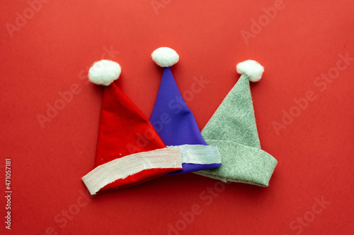 Flat lay composition of multi-colored Santa Claus caps on a red background. Place under text © Пётр Рябчун