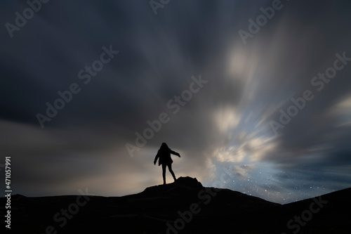 Silhouette of a person on a mountain top, long exposure clouds.