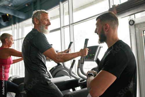 Cheerful mature man happily chatting with trainer while exercising