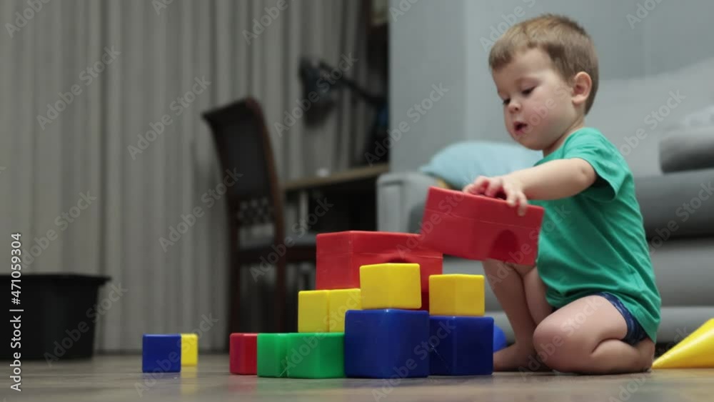 little kid boy building tower garage from colorful plastic cubes blocks on floor in living room. caucasian child in green shirt playing with toys at home, constructing, education, learning activity little kid boy building tower garage from colorful plastic cubes blocks on floor in living room. caucasian child in green shirt playing with toys at home, constructing, education, learning activity