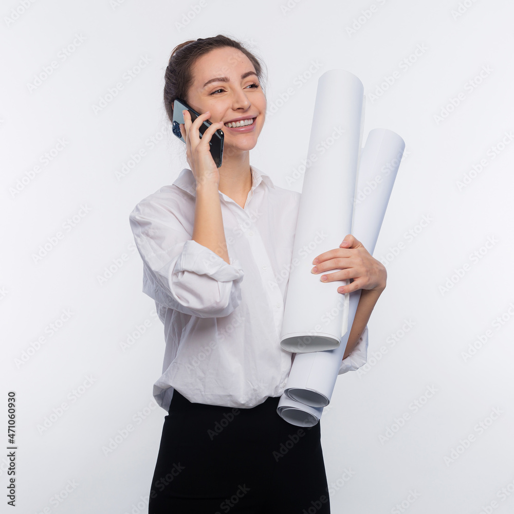 Young and cute business woman holds blueprints in her hand and use her phone. She is happy and shares the news on the phone her project was approved and she got the job isolated on white copy space Young and cute business woman holds blueprints in her hand and use her phone. She is happy and shares the news on the phone her project was approved and she got the job isolated on white copy space