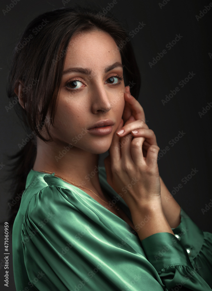 Portrait of a dark-eyed beautiful woman dressed in a green blouse, she has gold earrings and looks at camera against dark gray background, copy space Portrait of a dark-eyed beautiful woman dressed in a green blouse, she has gold earrings and looks at camera against dark gray background, copy space