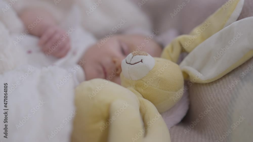 Close-up yellow bunny toy lying in bed with sleeping carefree Caucasian infant at background. Blurred little baby girl dreaming at home indoors. Innocence and infancy concept Close-up yellow bunny toy lying in bed with sleeping carefree Caucasian infant at background. Blurred little baby girl dreaming at home indoors. Innocence and infancy concept