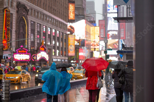 Some people are walking in Times Square during a rainy day. Times Square is a major commercial intersection  tourist destination in Midtown Manhattan.