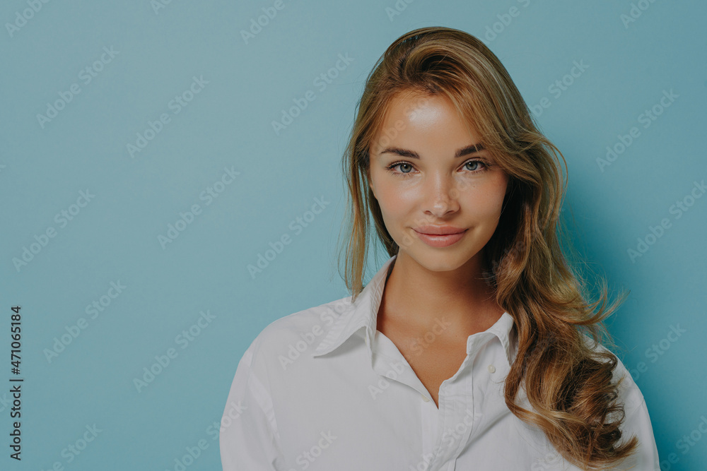 Portrait of young caucasian female model with dyed blonde hair smiling at camera on blue background Portrait of young caucasian female model with dyed blonde hair smiling at camera on blue background