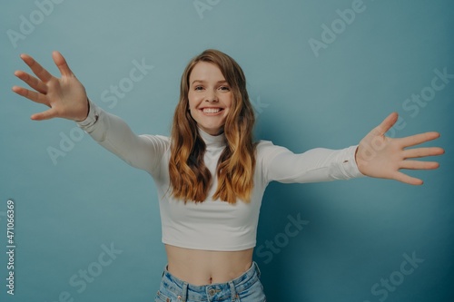 Overjoyed cheerful young woman with arms wide open outstretched to embrace hug someone