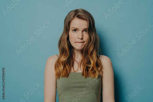 Quadro em tela Confused worried young woman with wavy hair biting lip and feeling guilty, isola